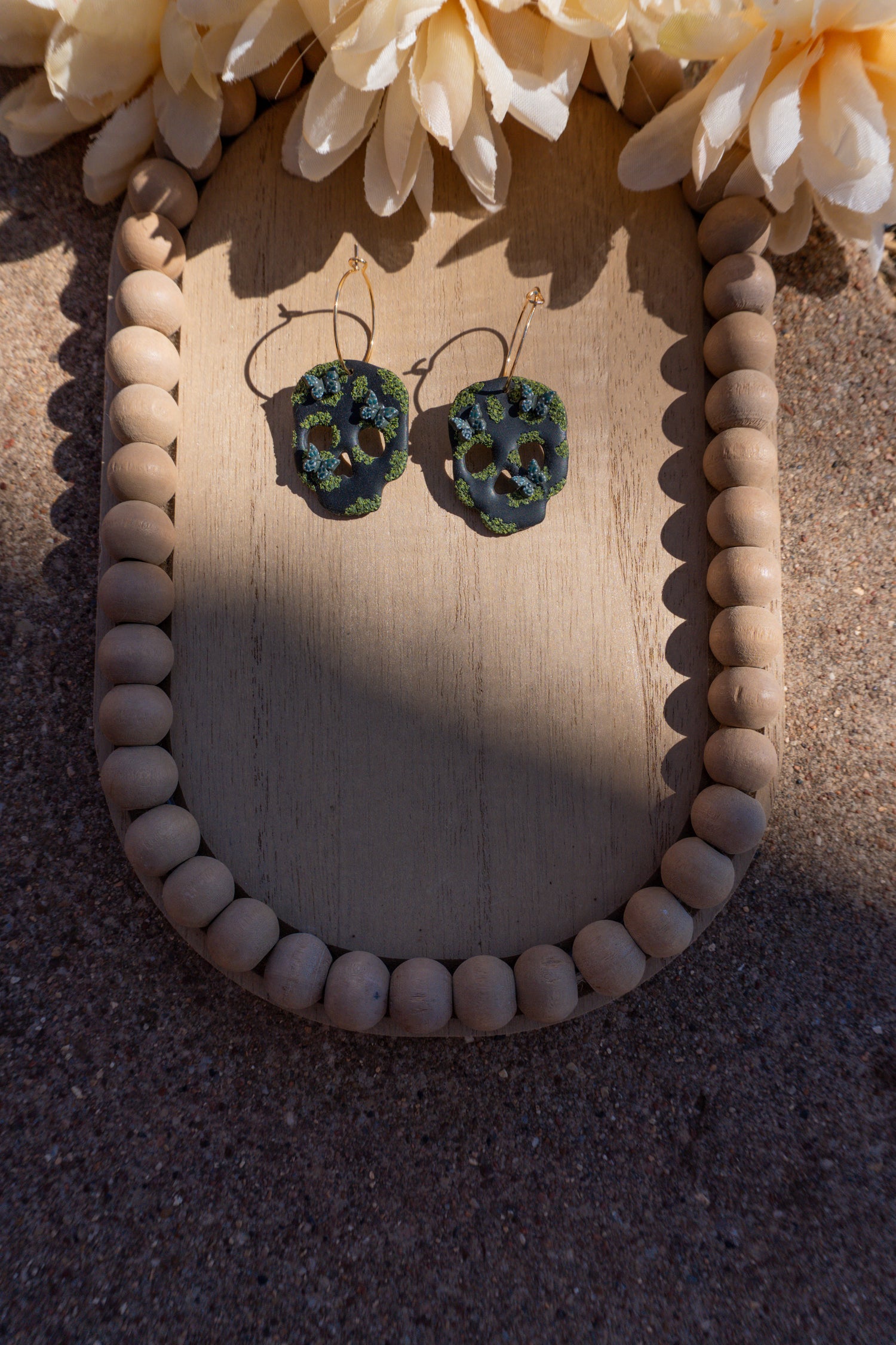 Skull earrings that are cottage-core themed, attached to gold hoop earring posts.