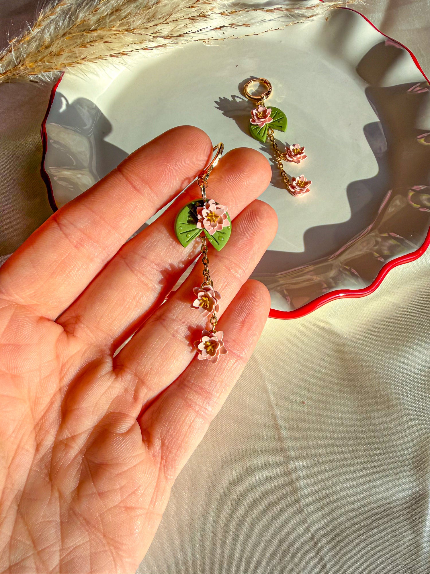 Hand holding a pair of lily pad floral earrings with a decorative plate in the background