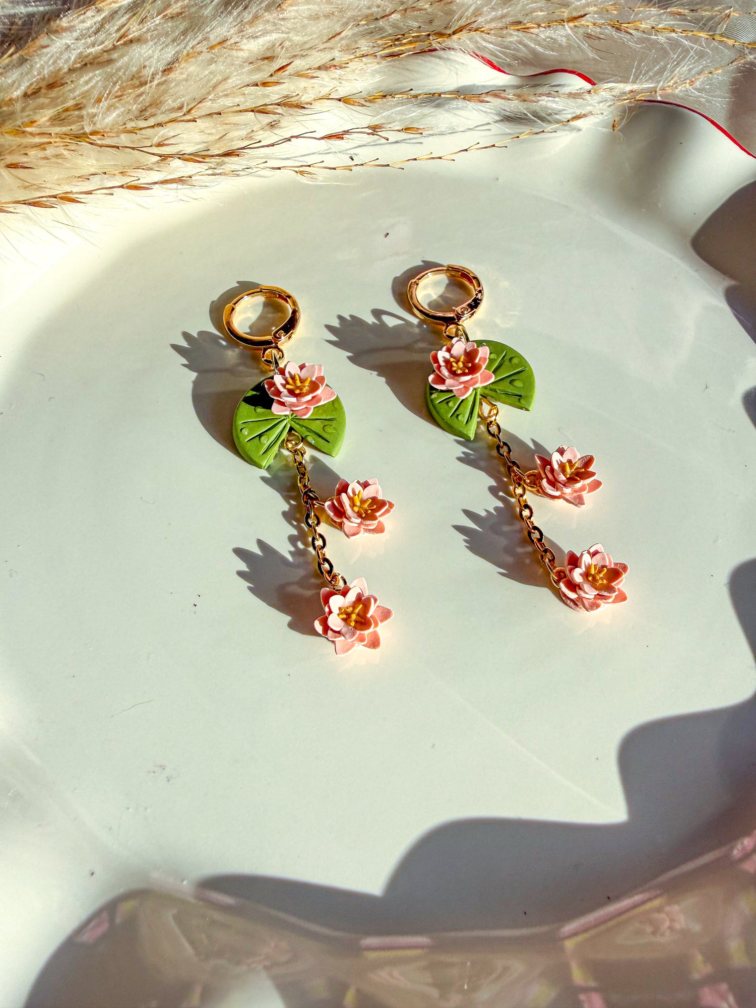 Green lily pads with pink lily flowers attached and dropping from earring. Displayed on white dish.