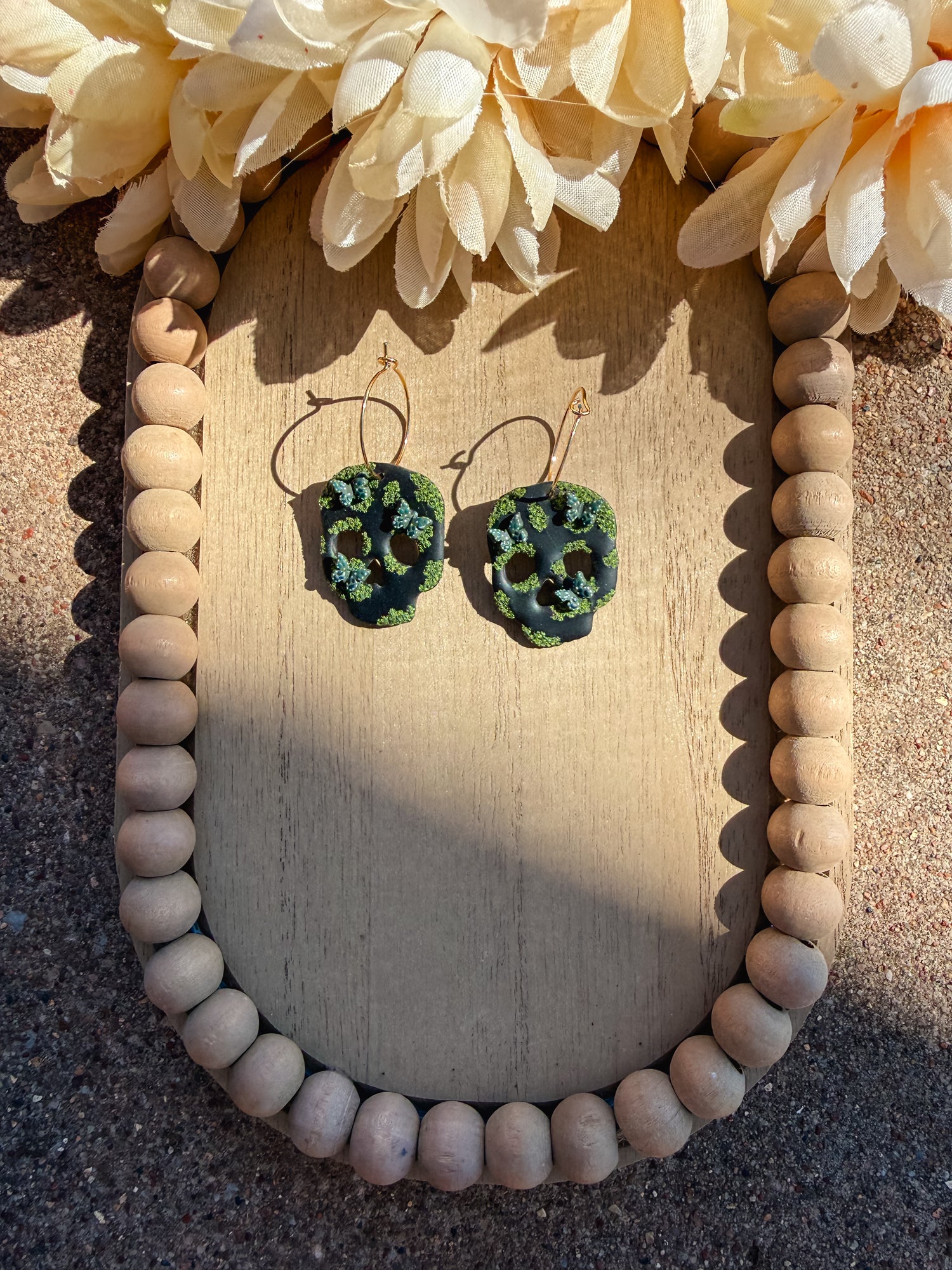 Gold hoop earrings with black skulls that have moss and butterflies on it.