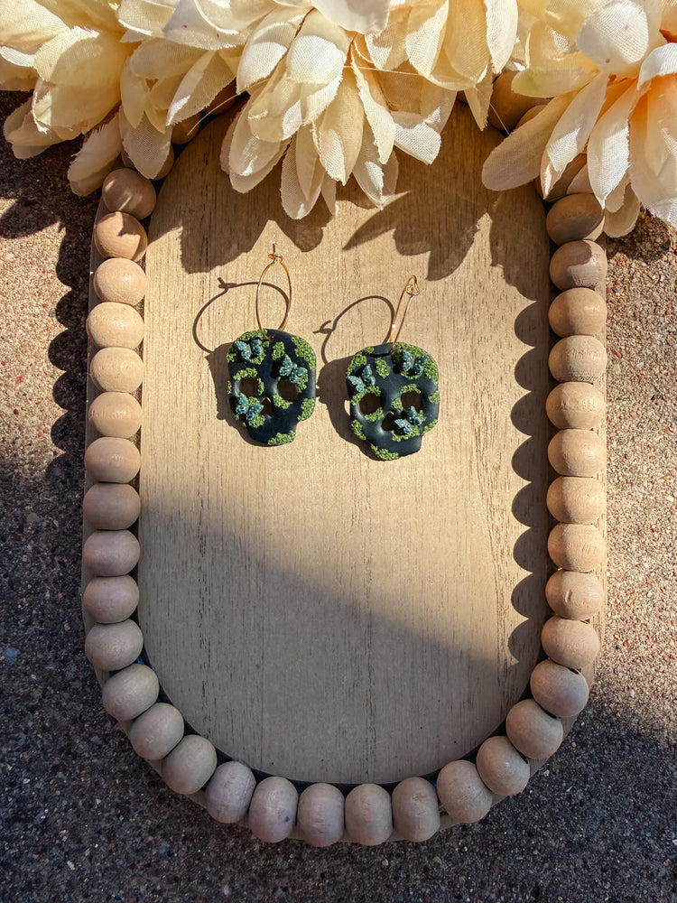 Gold hoop earrings with black skulls that have moss and butterflies on it.