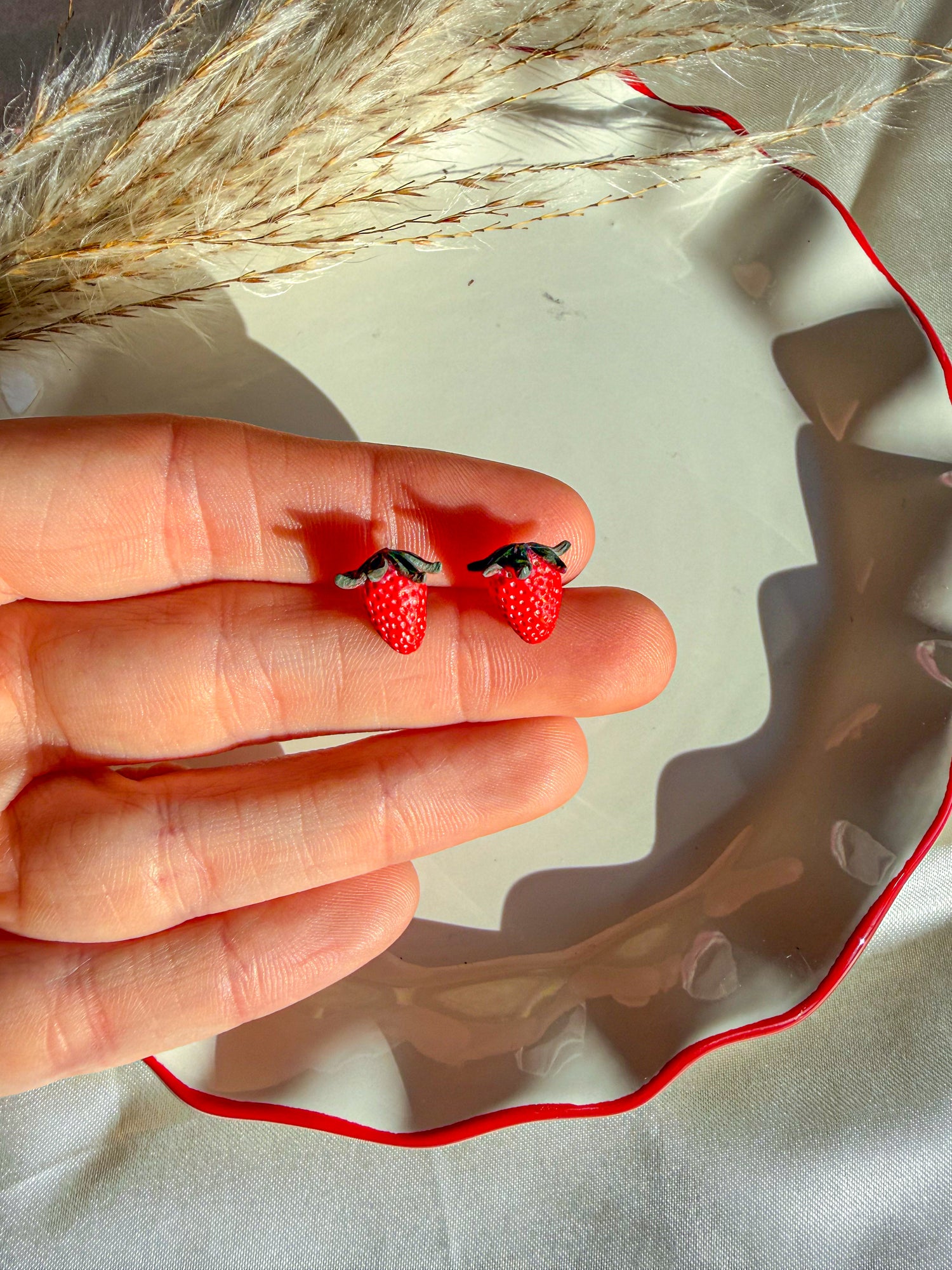 Hand holding strawberry stud clay earrings