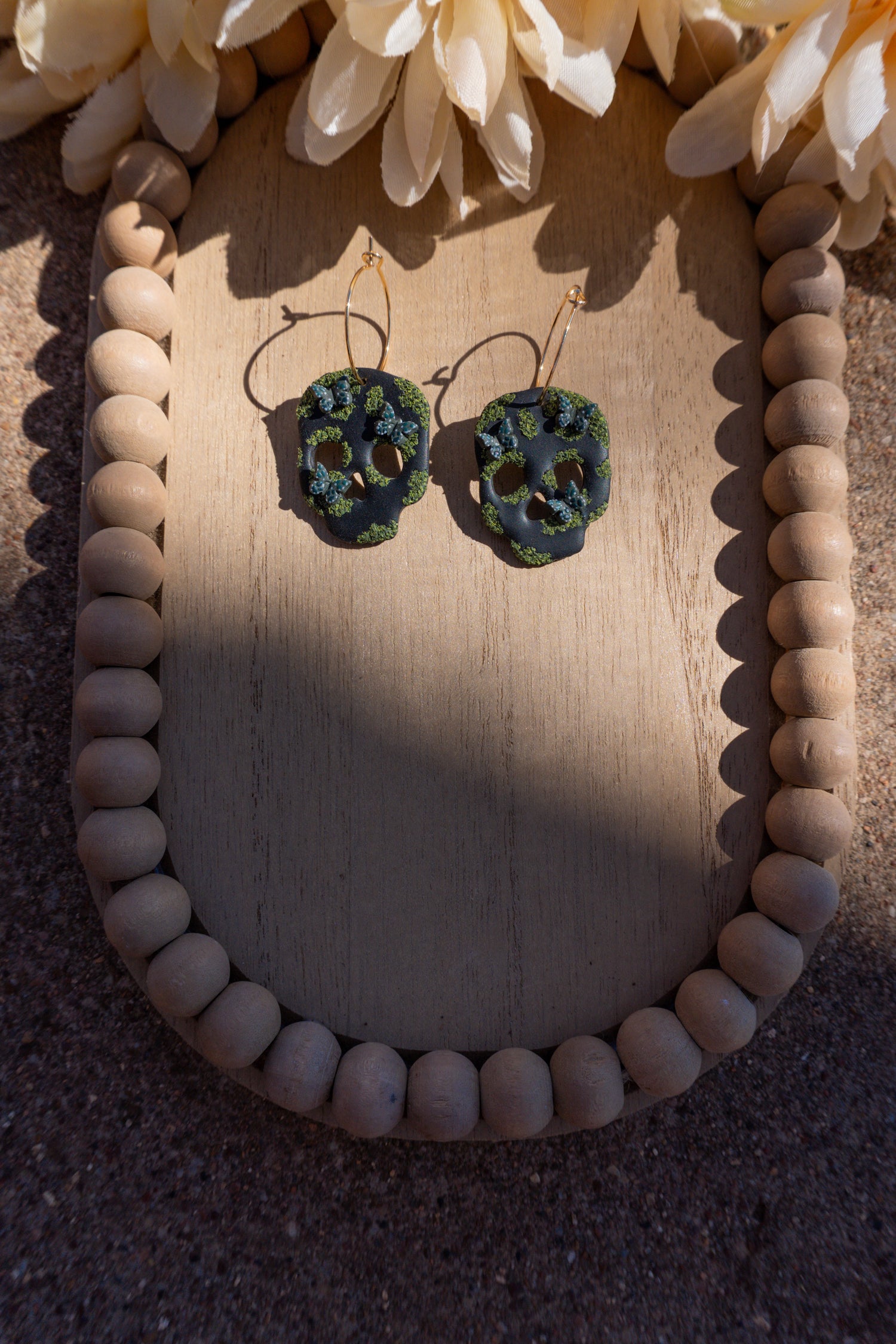 Pair of clay black skull earrings that have hunter green butterflies and green moss.