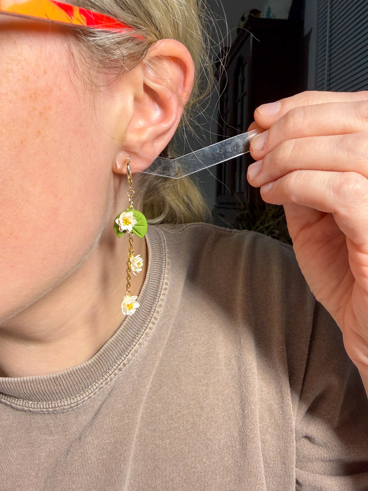 Person holding white lily pad earrings next to ear for size reference
