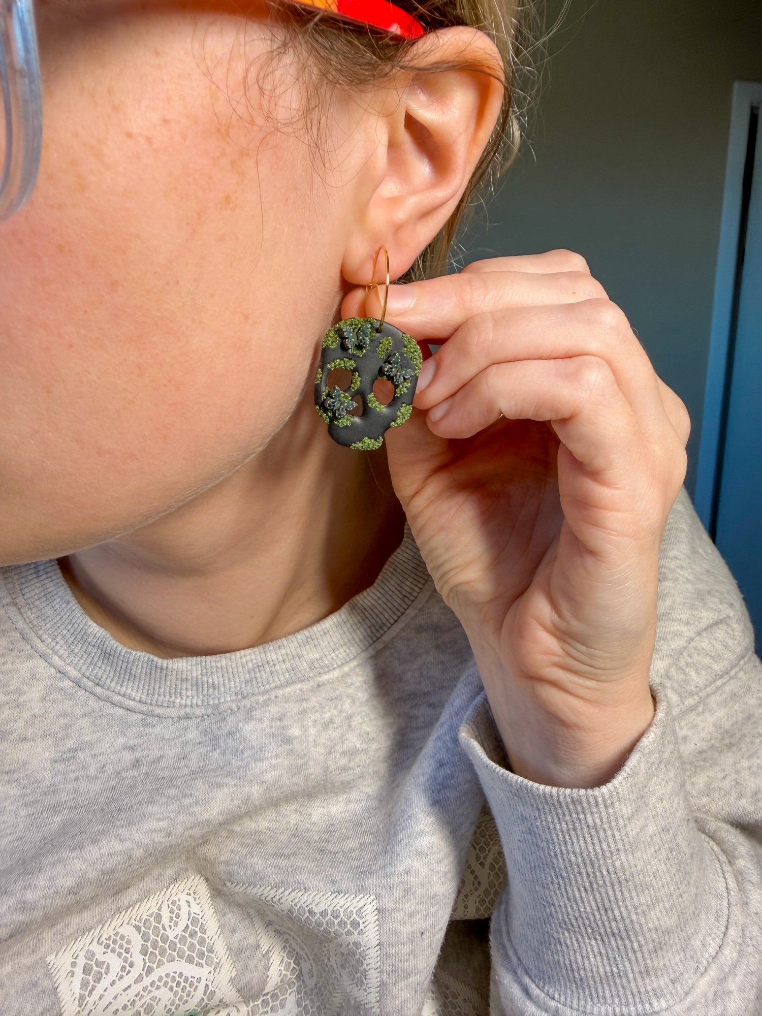 Person wearing black skull clay earrings with moss and dark green butterflies