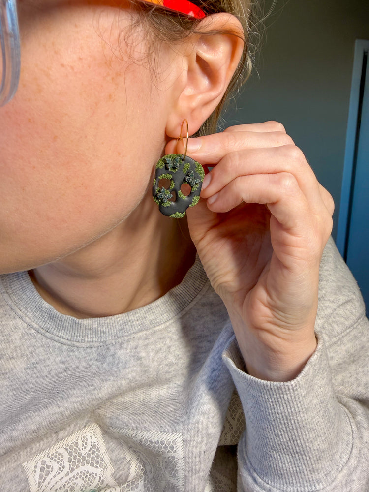 Person wearing black skull clay earrings with moss and dark green butterflies