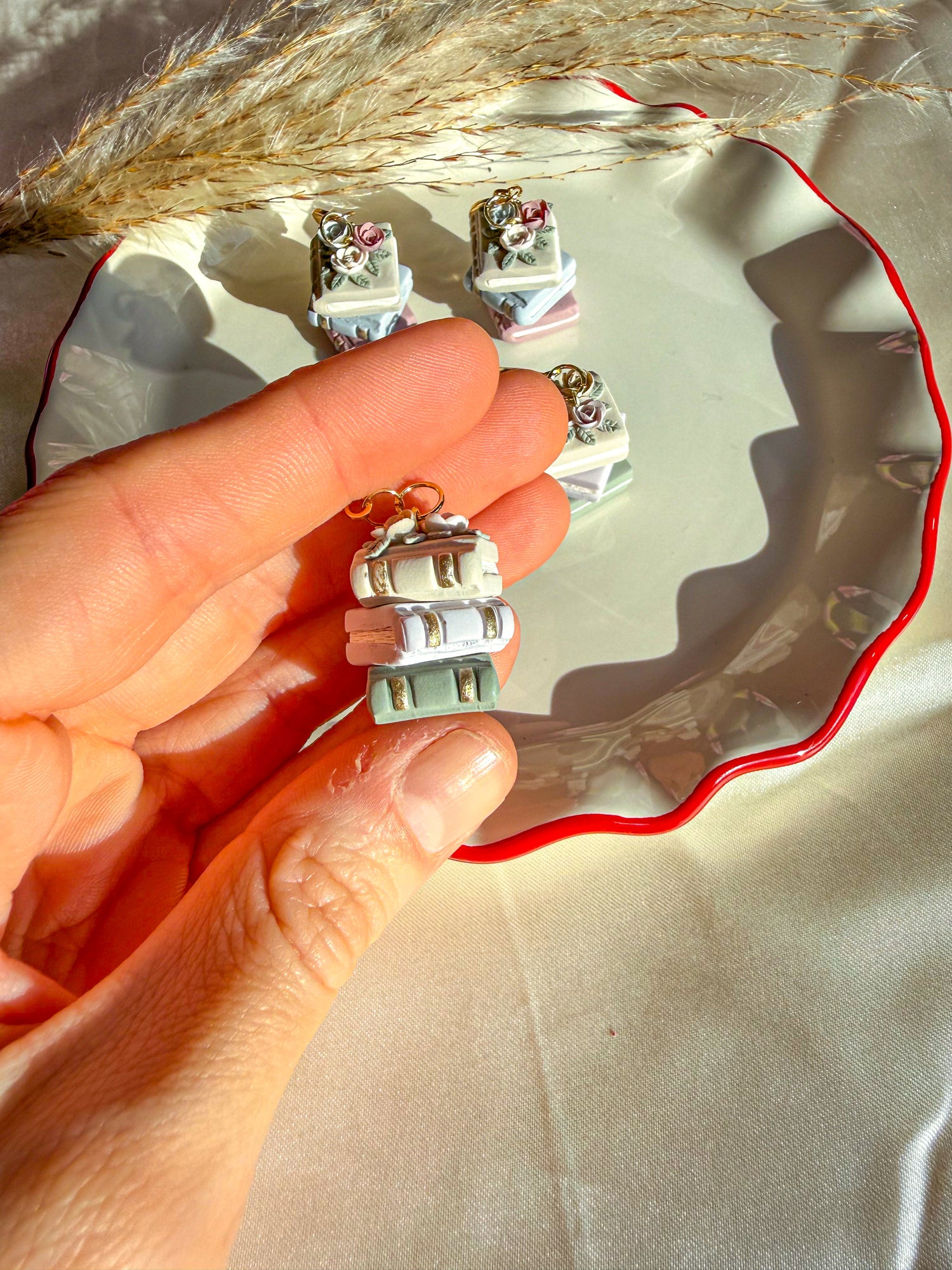 Hand holding neutral colored book stack earrings. Showing gold accents on the side of the earring/book.