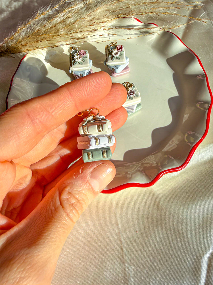 Hand holding neutral colored book stack earrings. Showing gold accents on the side of the earring/book.