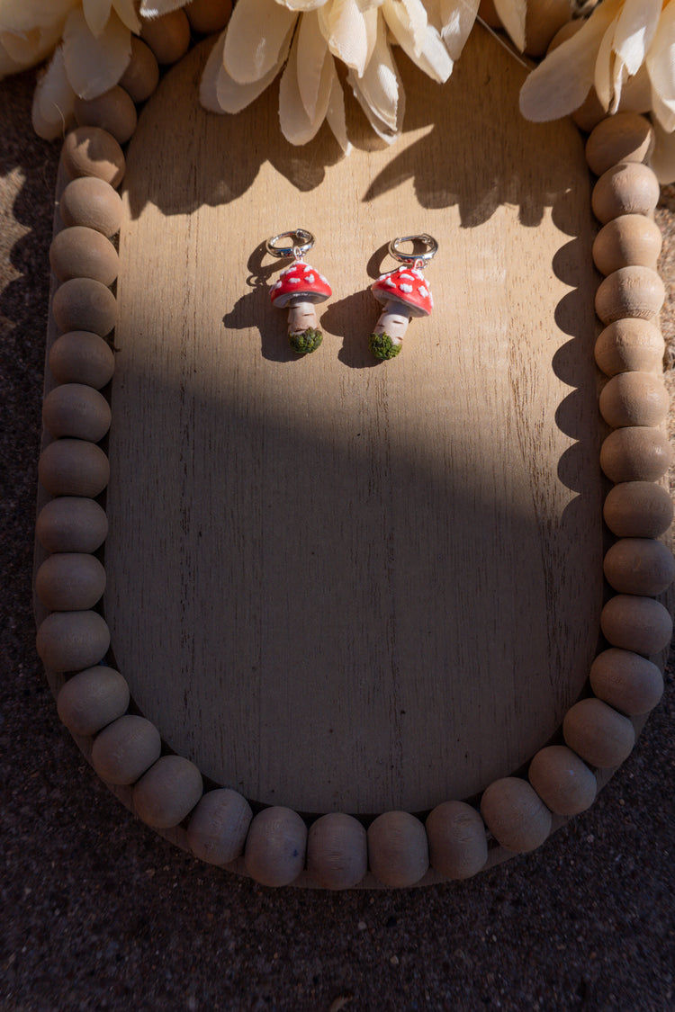 Mushroom-shaped earrings on a wooden surface with decorative elements.