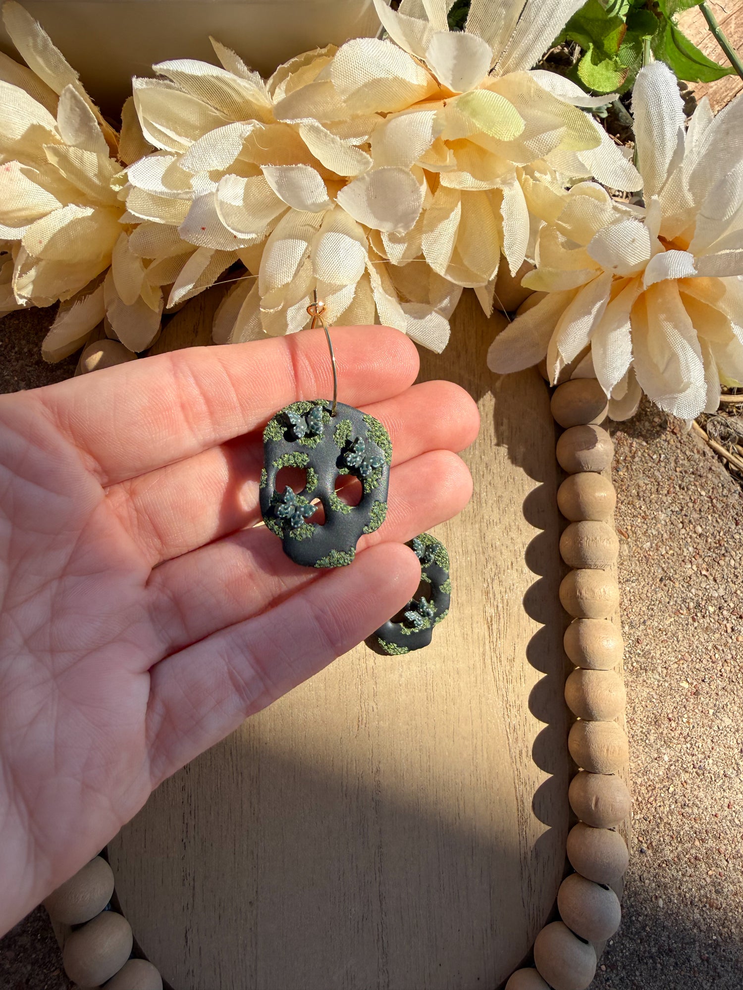 Hand holding black skull that has butterflies and green moss on it.