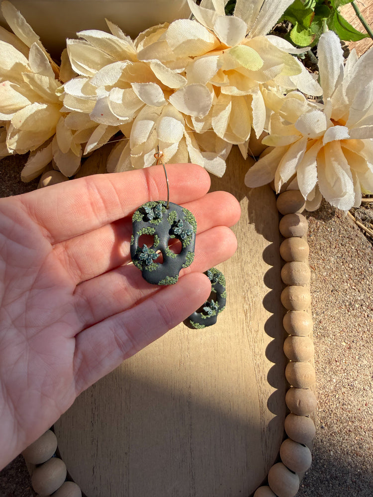 Hand holding black skull that has butterflies and green moss on it.