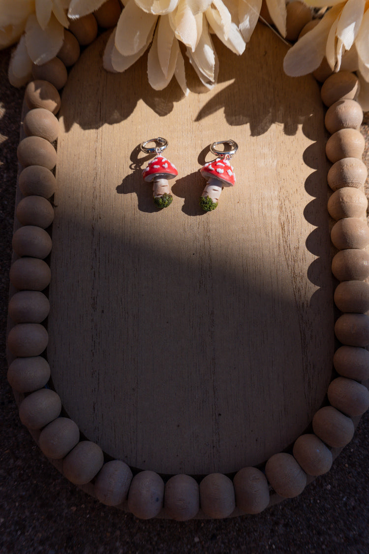 Pair of mushroom-shaped earrings on a wooden surface with decorative elements.