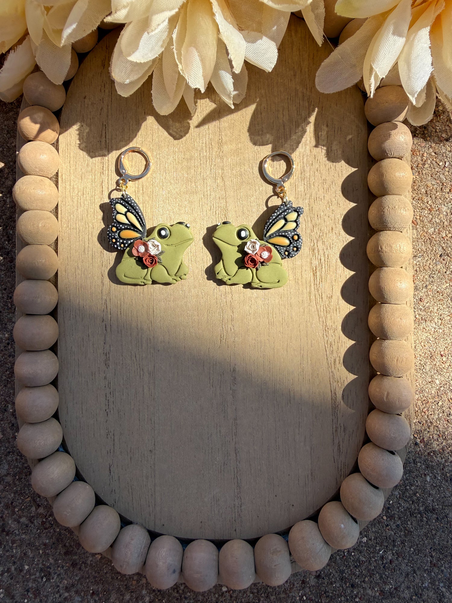 Frog earrings with monarch wings and neutral flowers on frogs body