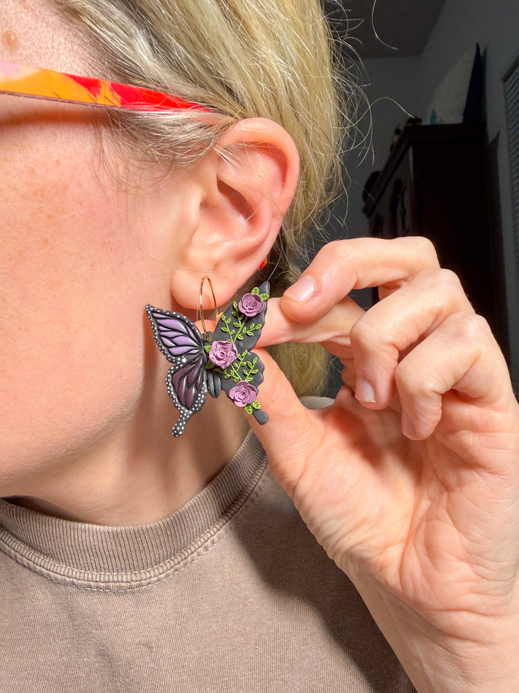 Person wearing a butterfly earring with floral details, adjusting it with their hand.