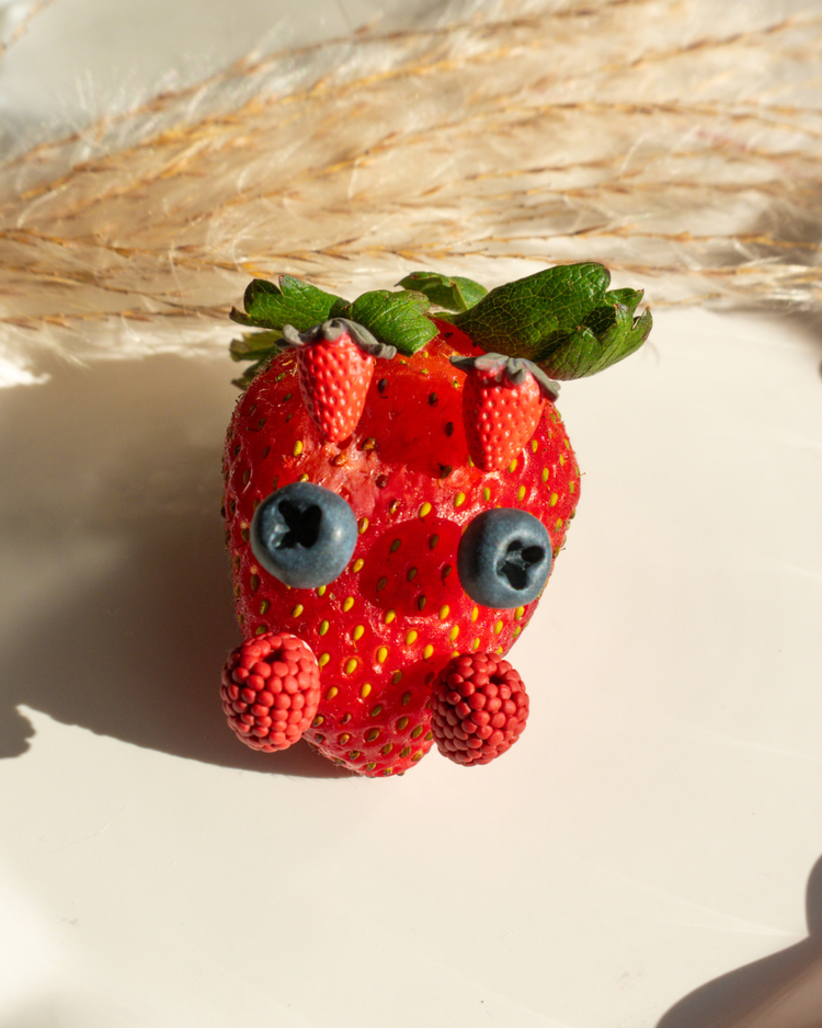 strawberry, blueberry, and raspberry stud earrings propped on a strawberry prop
