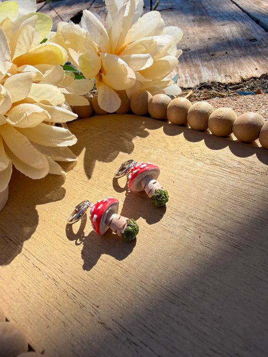 Mushroom-shaped earrings on a wooden surface with flowers in the background